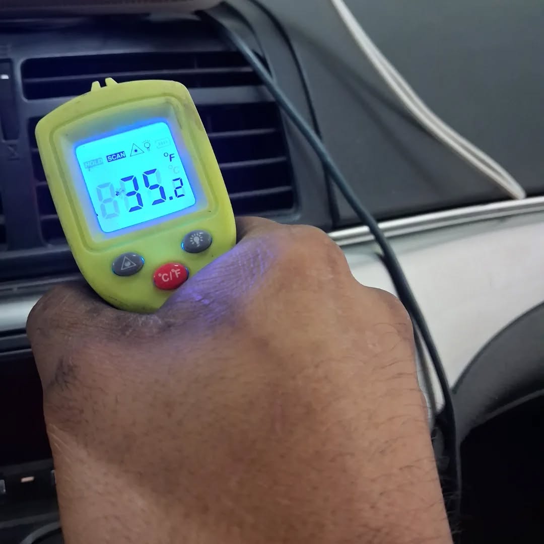 Mechanic testing vehicle A/C vent temperature with an infrared thermometer